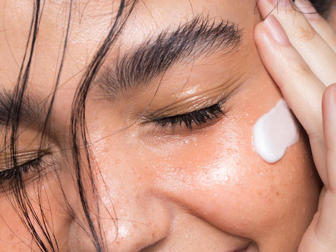 A closeup photo of a model applying cream on her cheek Desktop