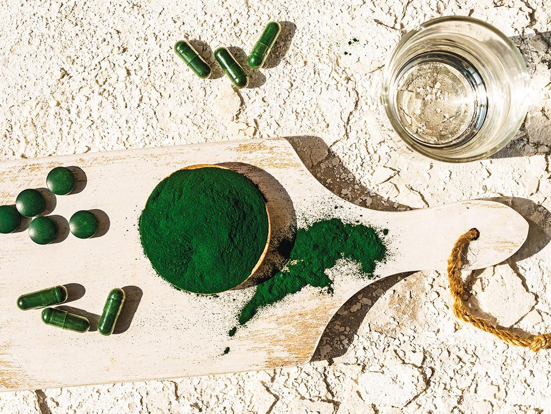 A photo of green algae powder in pills and capsules with a glass Desktop