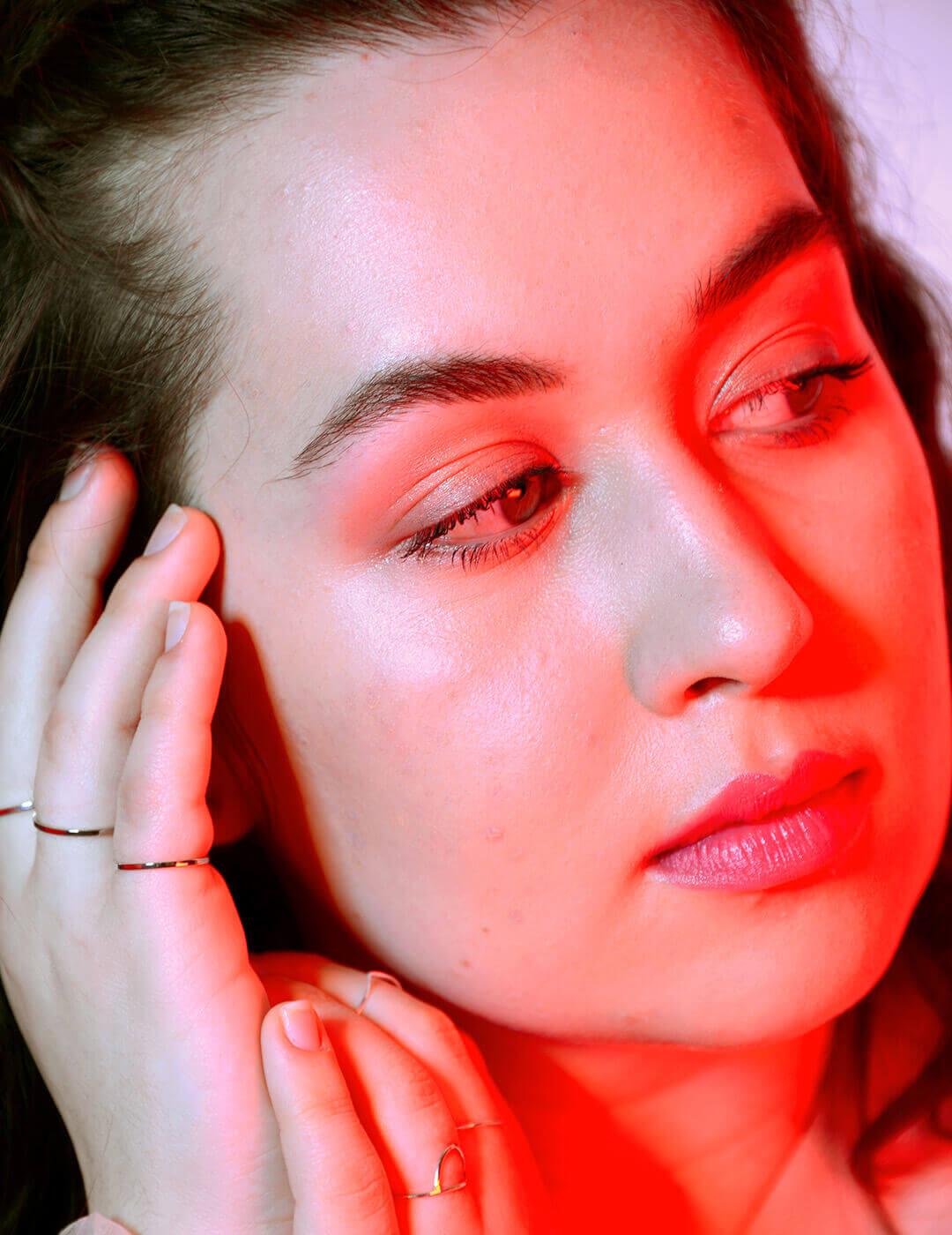 A close-up photo of a woman with intradermal fillers looking sideways, wearing thin gold rings on her fingers Mobile