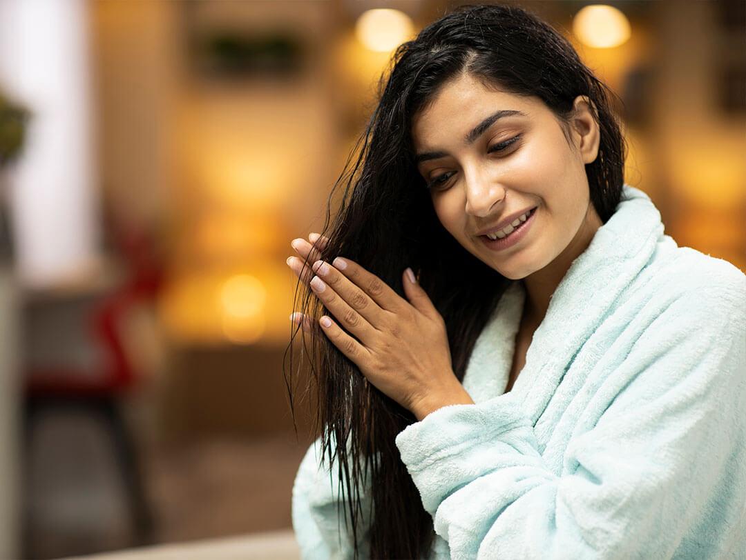 A picture shows a woman wearing a light blue bathrobe and oiling her hair after getting out of the shower Desktop