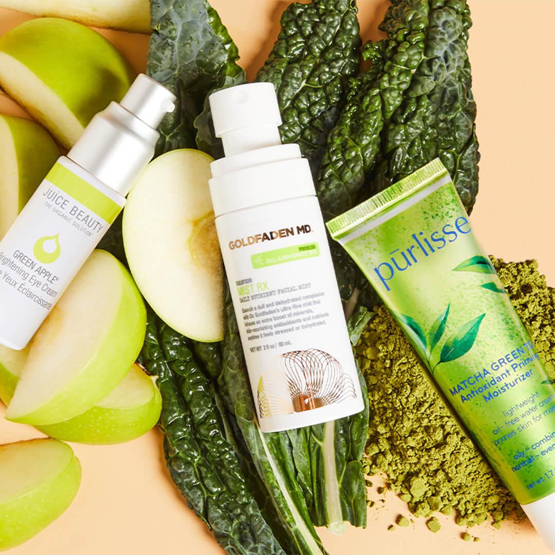 Skincare products from various brands on top of green apple slices, kale leaves, and matcha powder against cream background Mobile