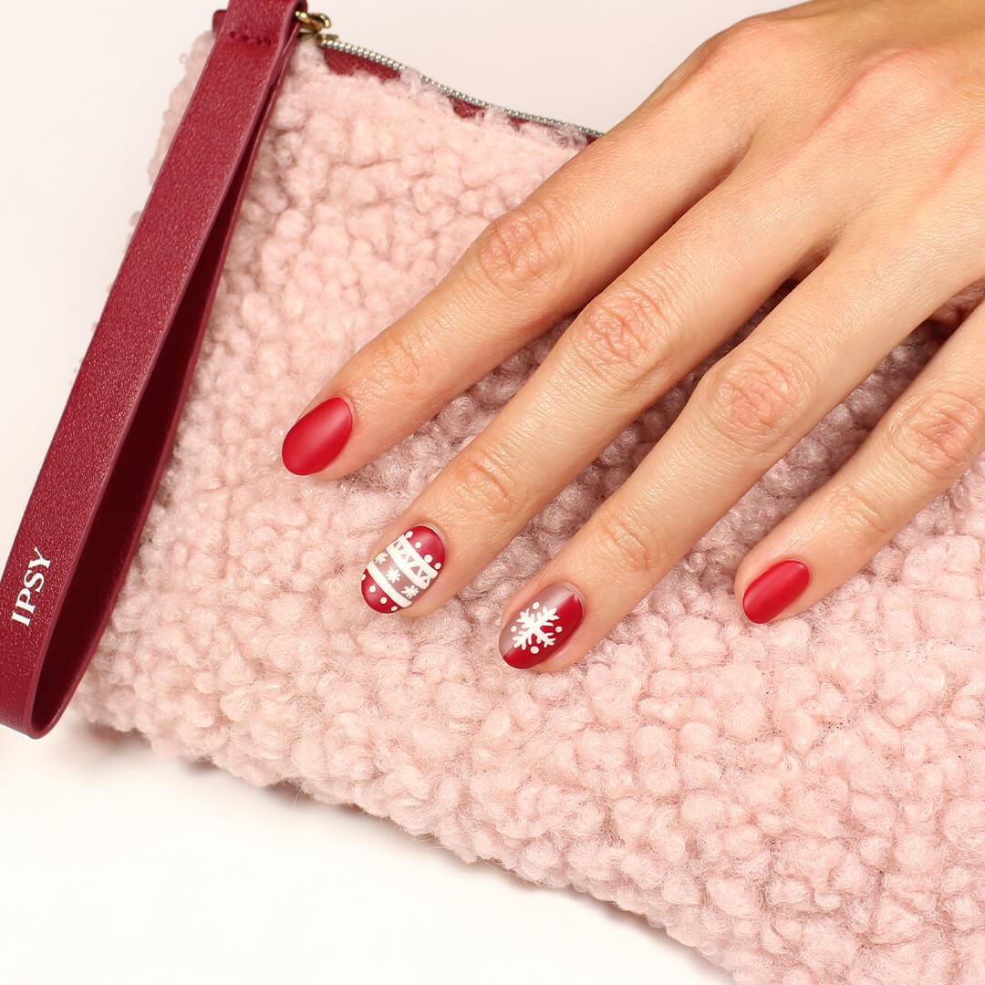 Image of a model's hand with red and white, holiday-themed nail art mani holding the December 2020 IPSY Glam Bag Desktop