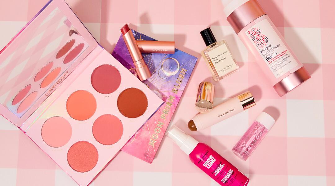 Skincare and makeup products from various brands scattered on pink background Desktop