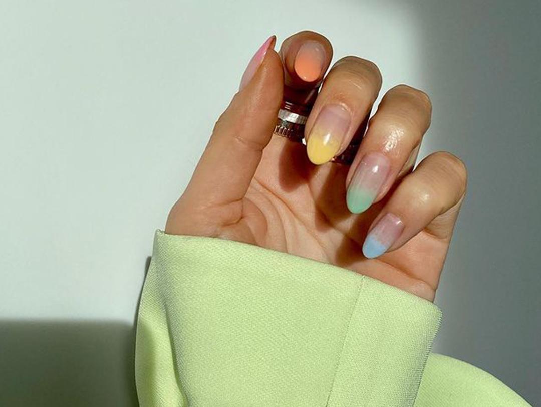 A closeup of a model's hand with a faded pastel rainbow nail polish Desktop