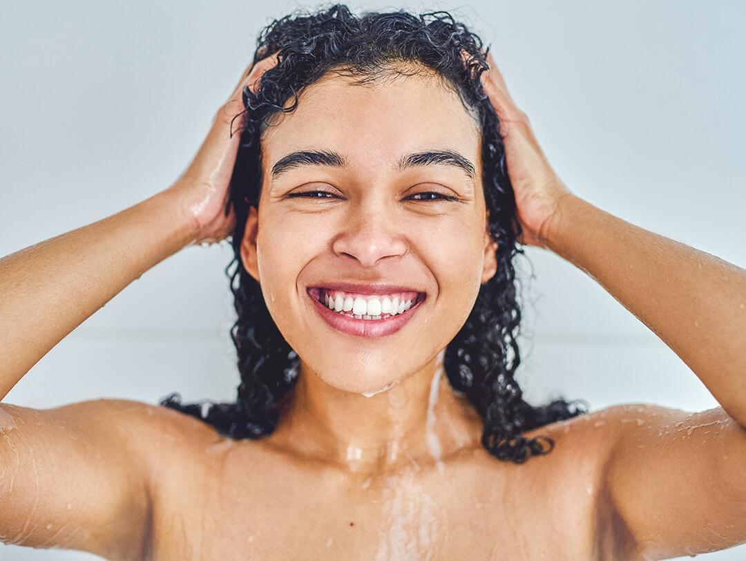 Close-up image of a smiling woman with curly hair taking a shower in her bathroom Desktop