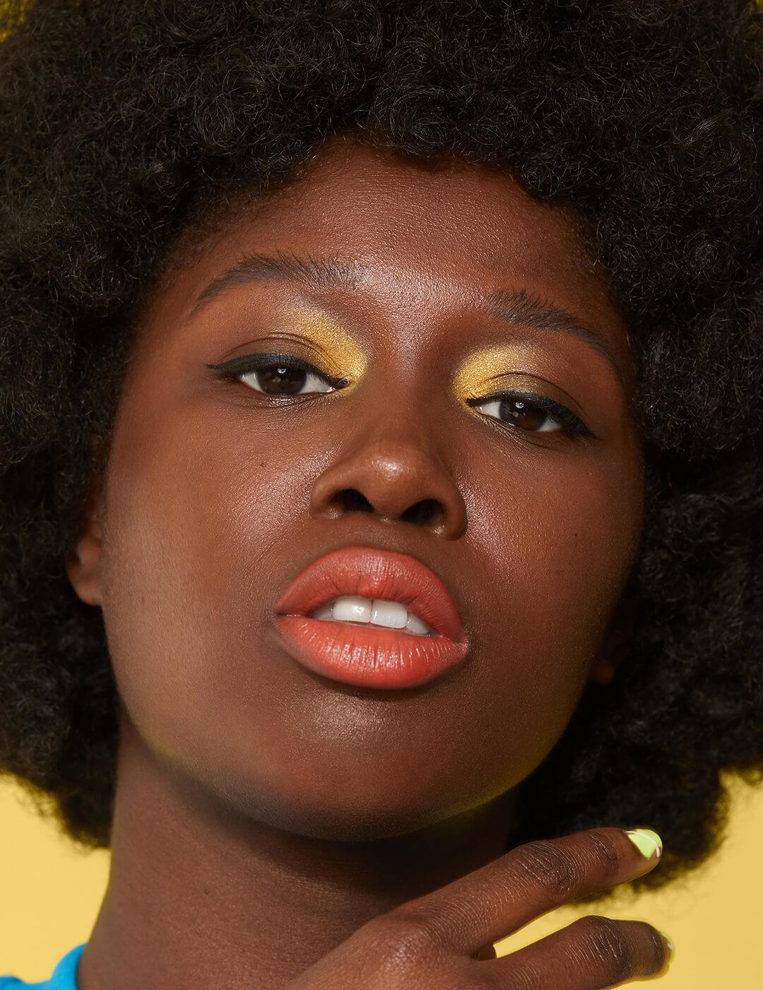 Close-up of a Black model rocking gold eyeshadow and orange lips Desktop