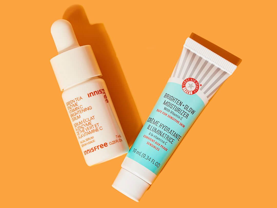 Various skincare products with vitamin C from various brands on orange background Desktop