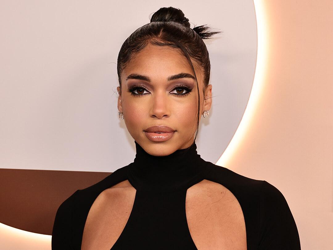 A photo of Lori Harvey with an espresso makeup look wearing a black dress on a beige background Desktop