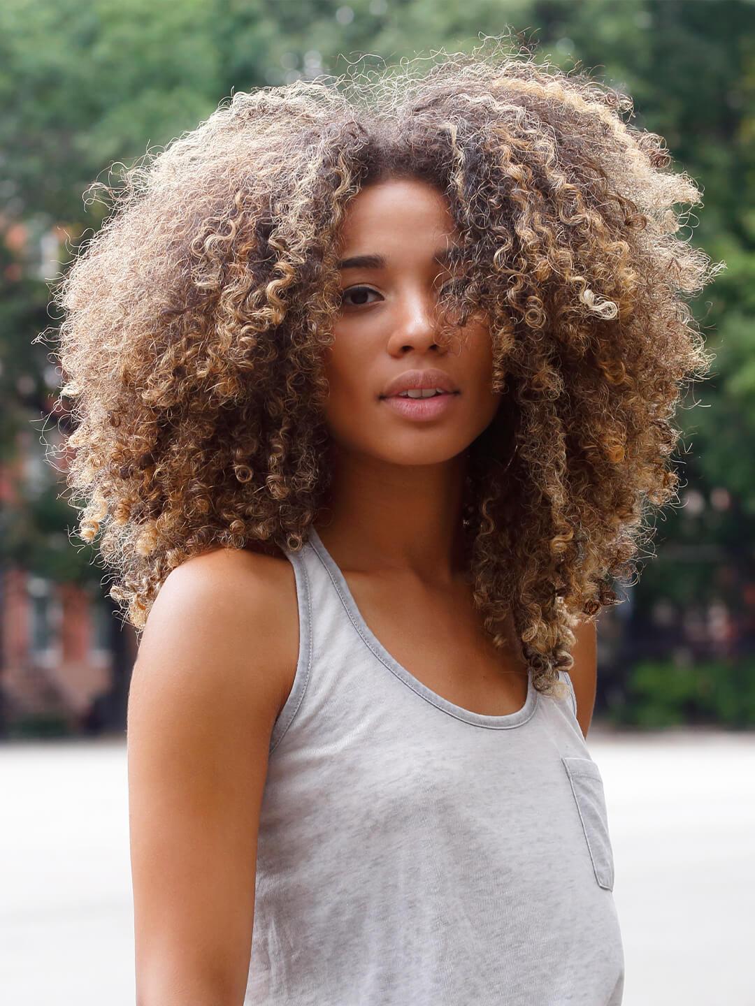 A young Latina female with afro looking at camera wearing summer clothes, in the park. Desktop