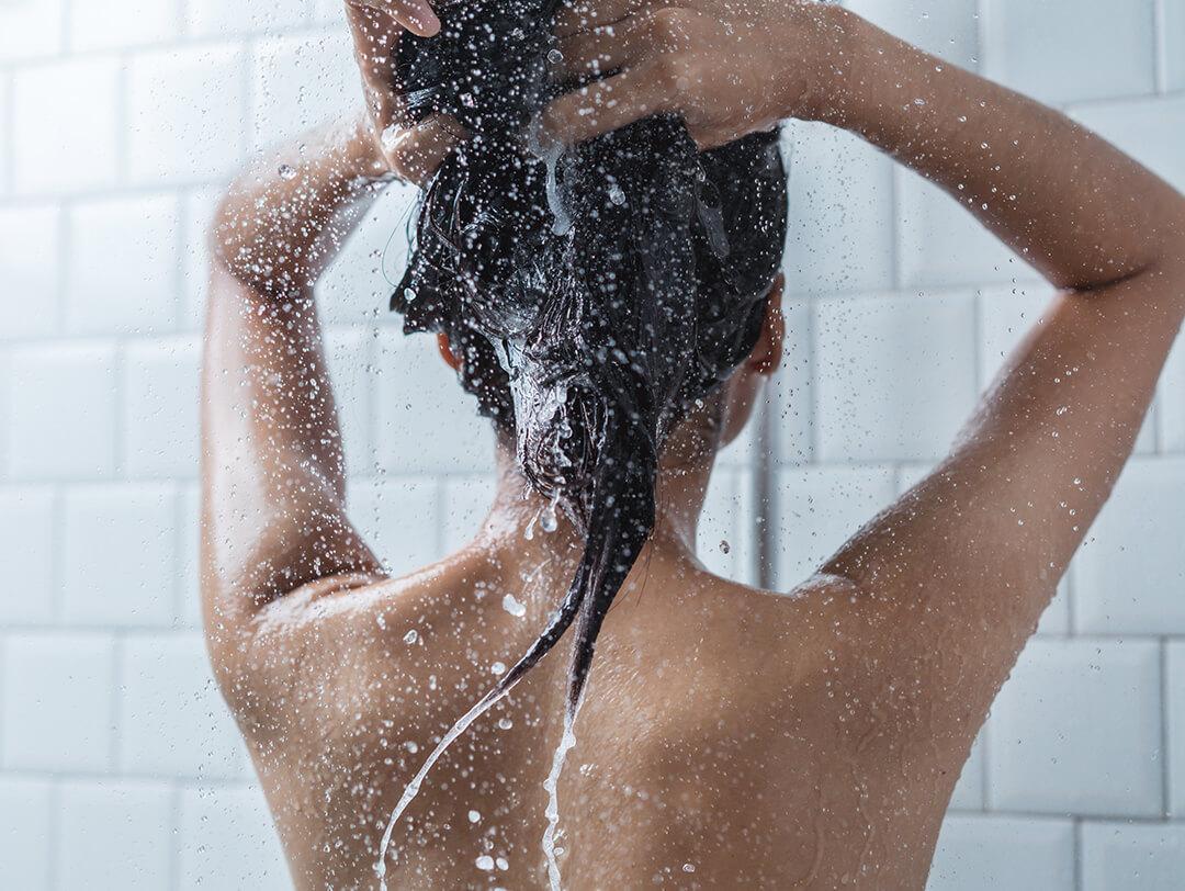 A photo of a shirtless woman showing her back while taking a shower against a white background Desktop