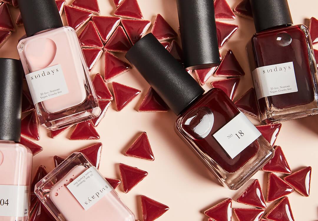 SUNDAYS Nail Polish in shades No. 04 and No. 18 on top of tiny red triangle tiles against cream background Desktop