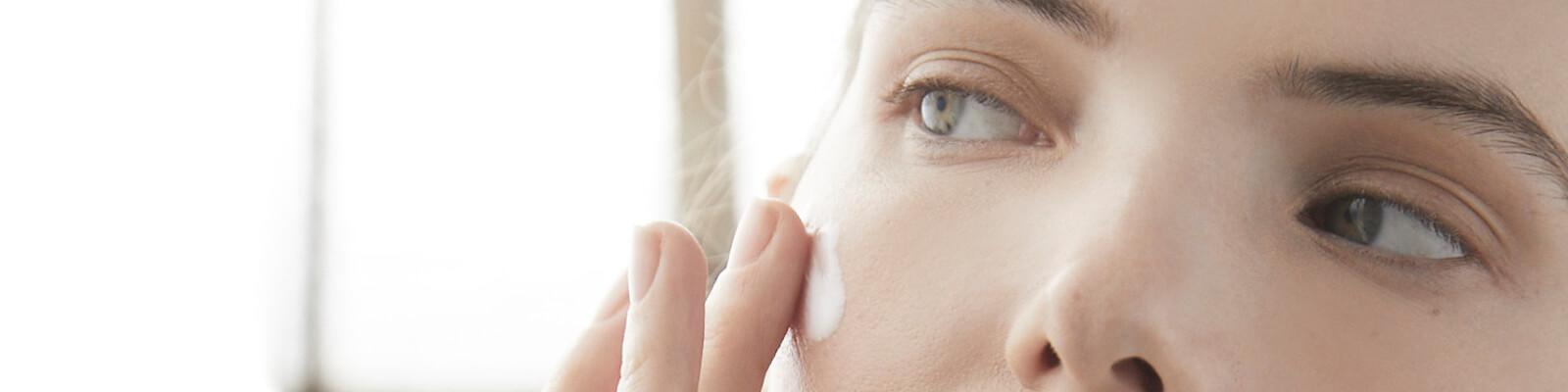 A closeup image of a model with neutral eyeshadow look putting cream on her cheek Desktop