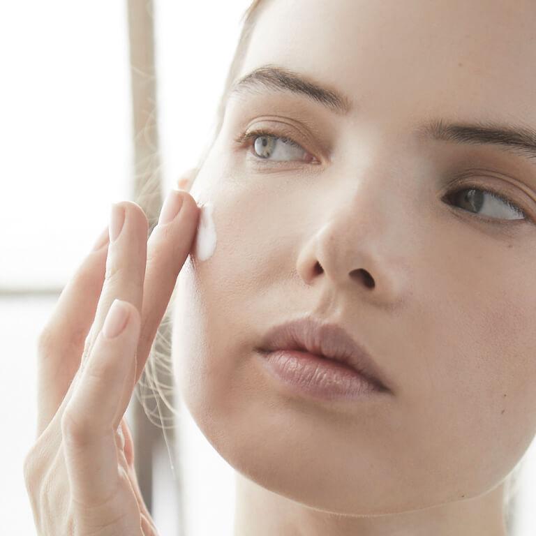 A closeup image of a model with neutral eyeshadow look putting cream on her cheek Mobile
