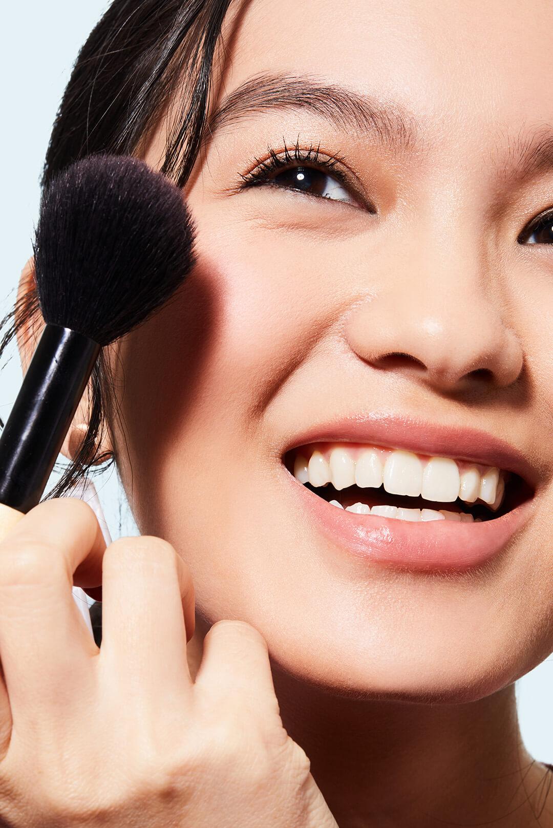 A photo of a smiling woman holding a makeup brush against a white background Desktop