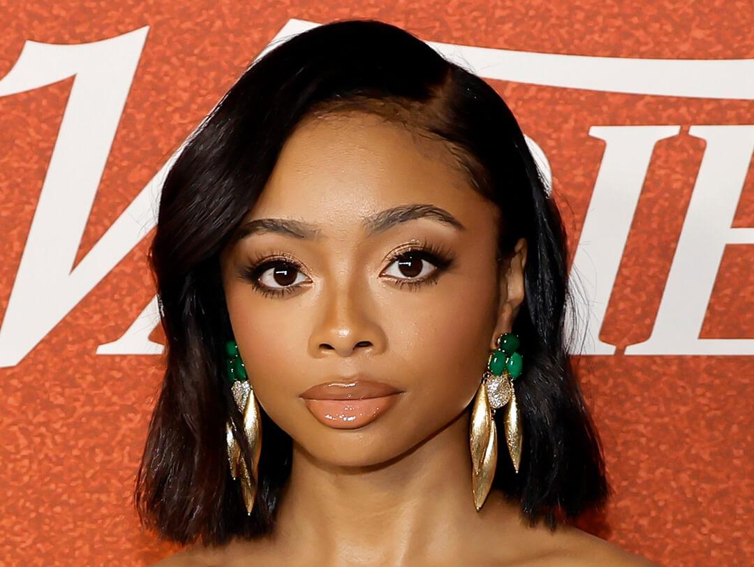 An image of Skai Jackson donning medium-length black hair while sporting a natural-toned lip color, alongside striking jade and golden drop earrings Desktop