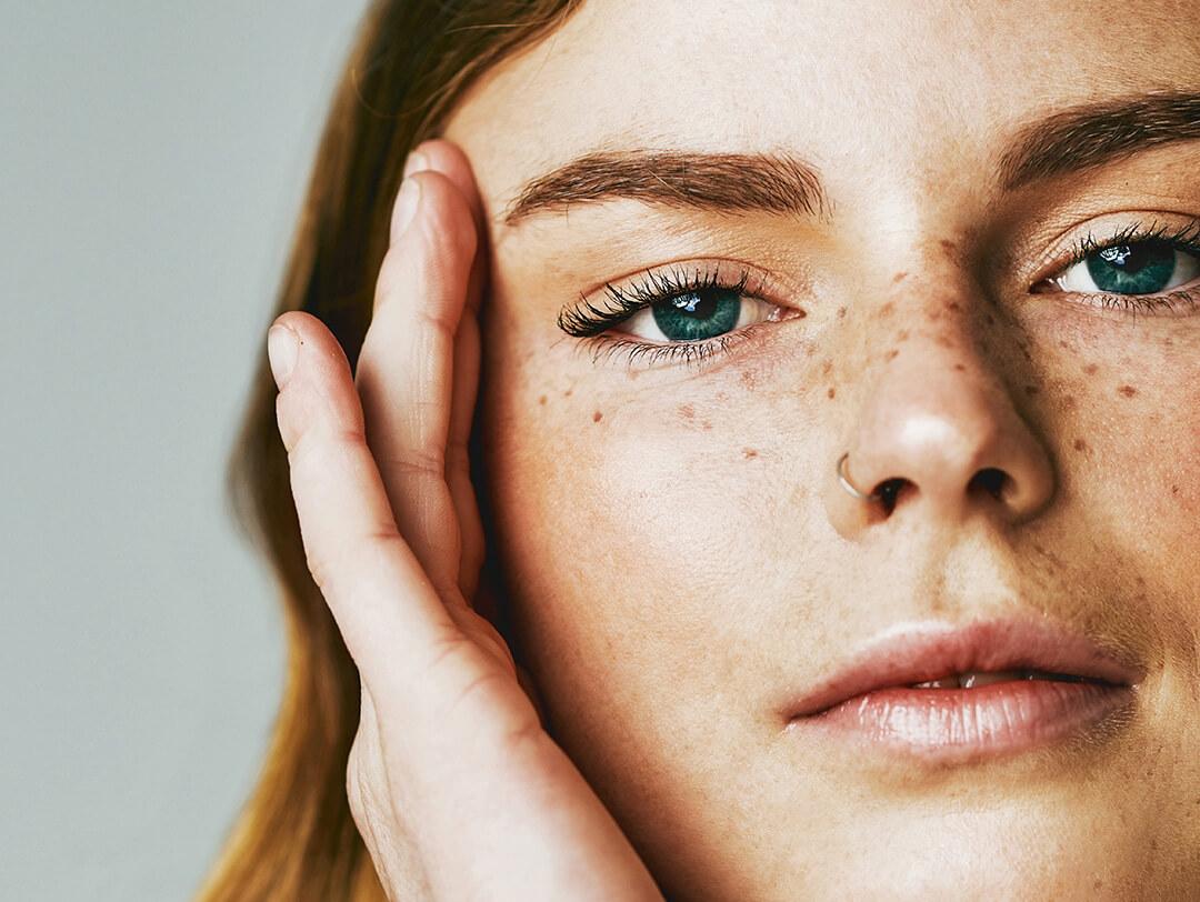 A closeup photo of a model posing and showing her natural skin against a grey background Desktop
