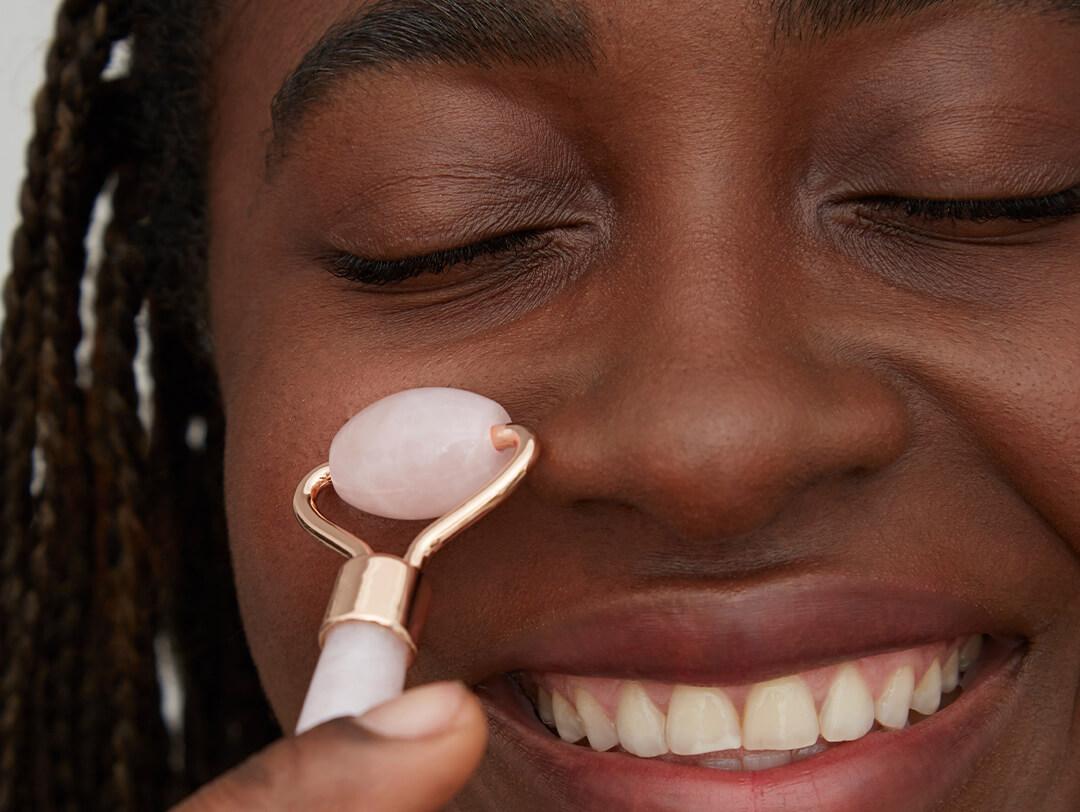 Close-up of a smiling Black woman using a quartz face roller under her eyes Desktop