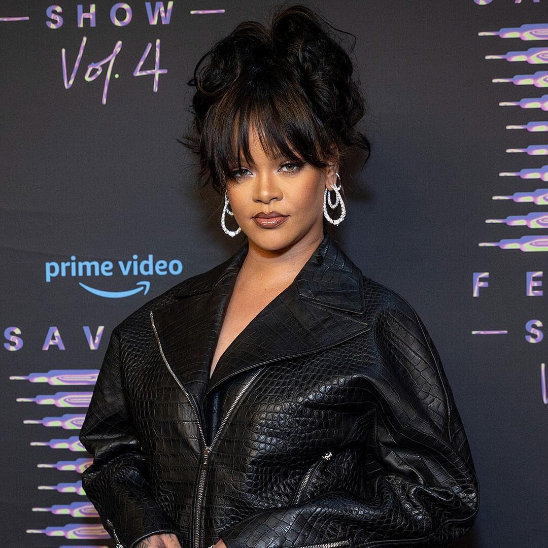 A photo of Rihanna with her hair up in a messy bun, a huge diamond ring and large hanging earrings, all done in matte monochrome makeup Mobile