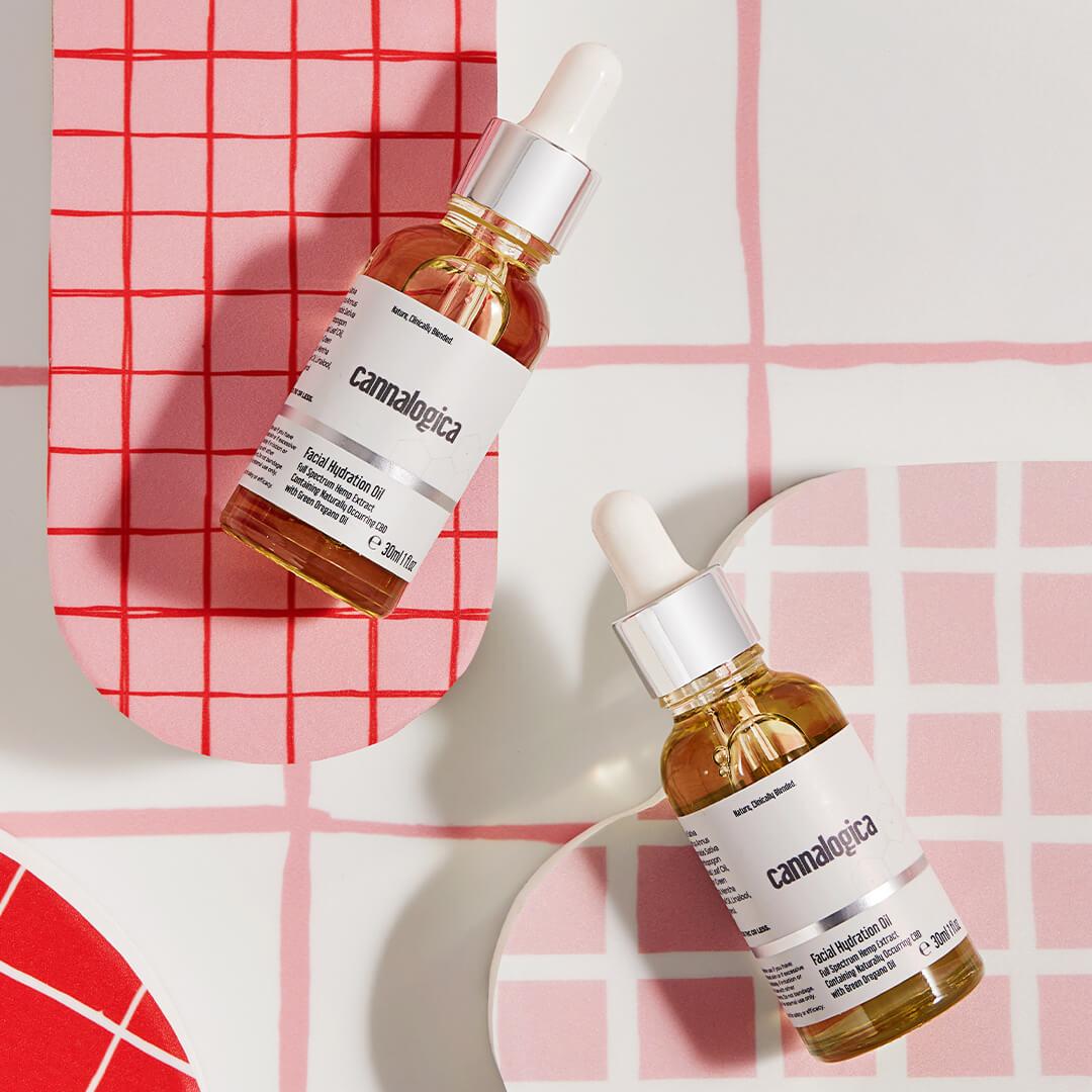 Flat-lay image of 2 bottles of CANNALOGICA Facial Hydration Oil on pink and white tiles background Desktop
