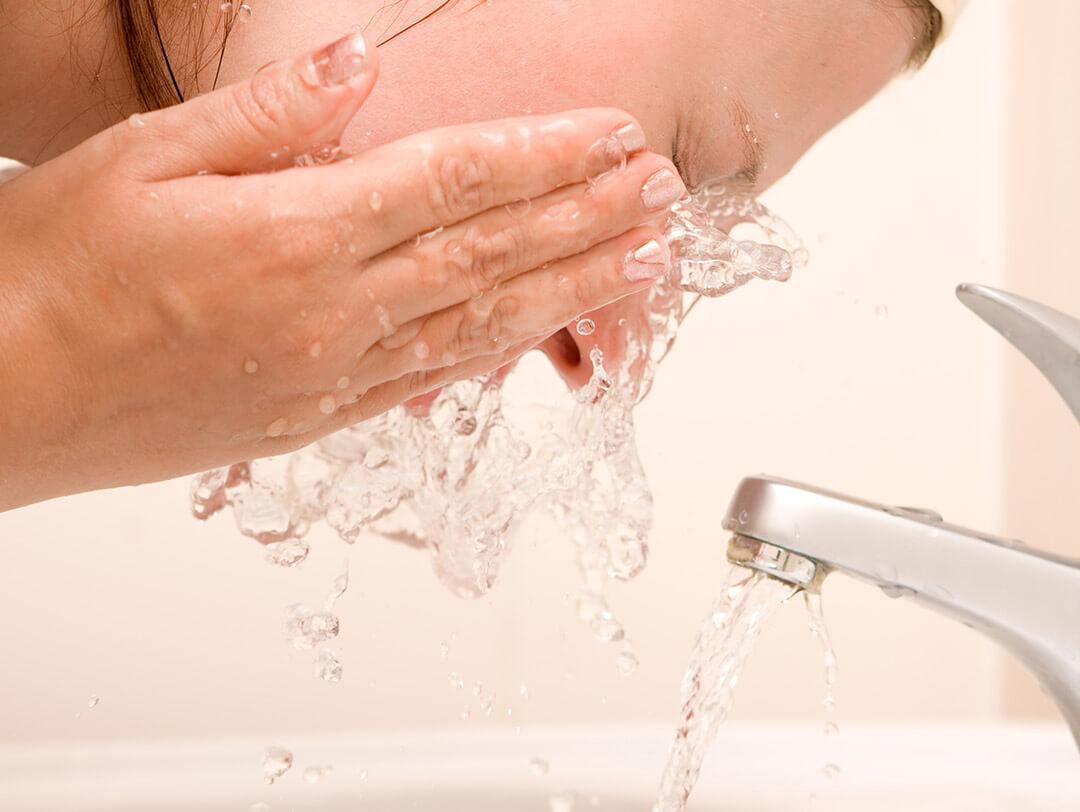 Close-up of a woman splashing water on her face near the faucet Desktop