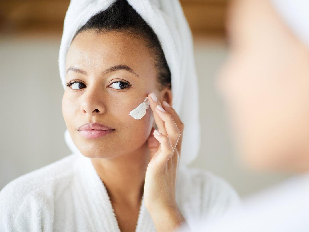 Woman in a bathrobe applying cream on her face while looking at herself in the mirror Desktop