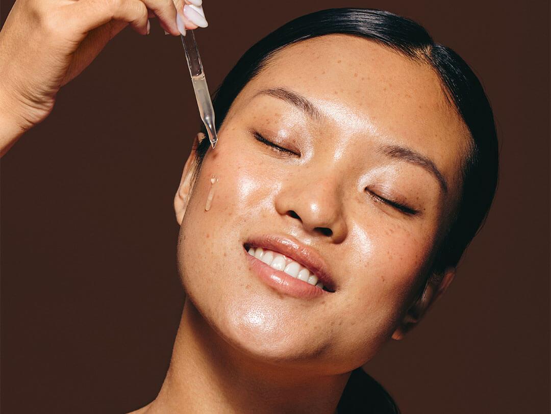 Woman with olive skin indulges in skincare routine using facial serum Desktop