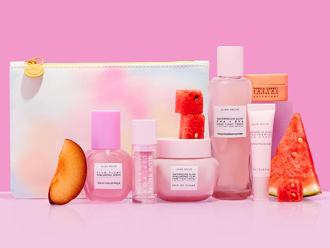 Various GLOW RECIPE beauty products with watermelon and peach slices and colorful makeup pouch on pink background Desktop