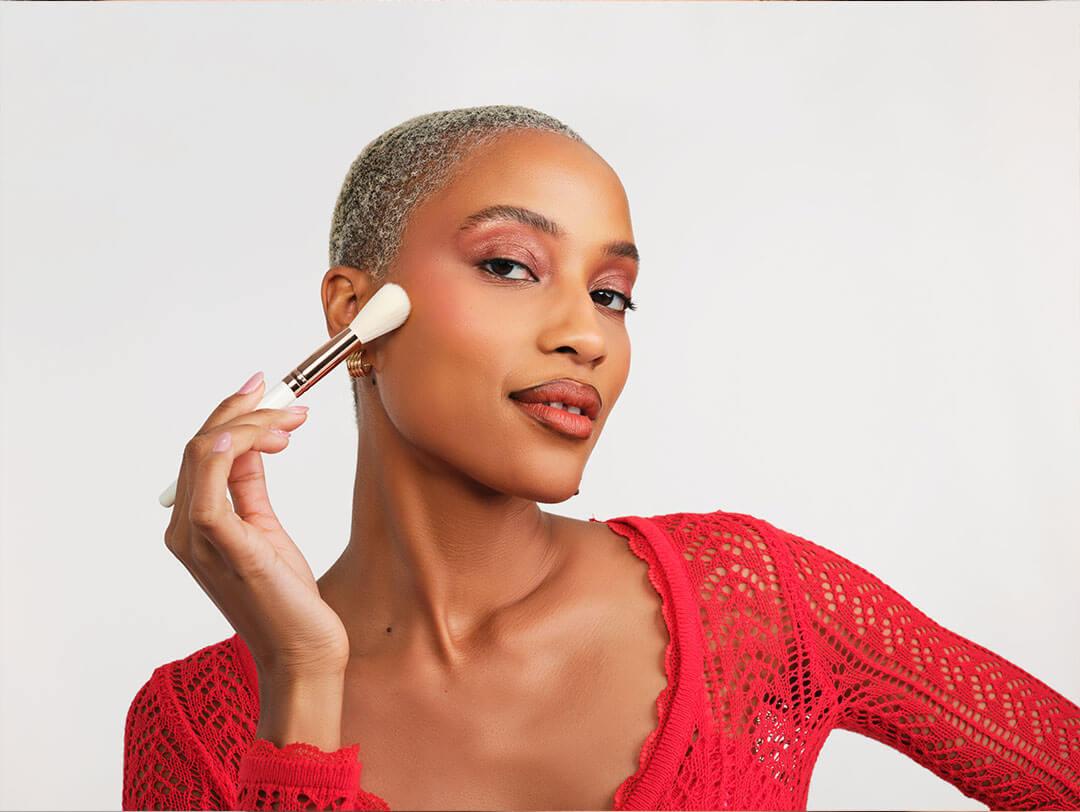 Woman demonstrates the precise application of blush on her cheeks to achieve a contoured radiant appearance Desktop