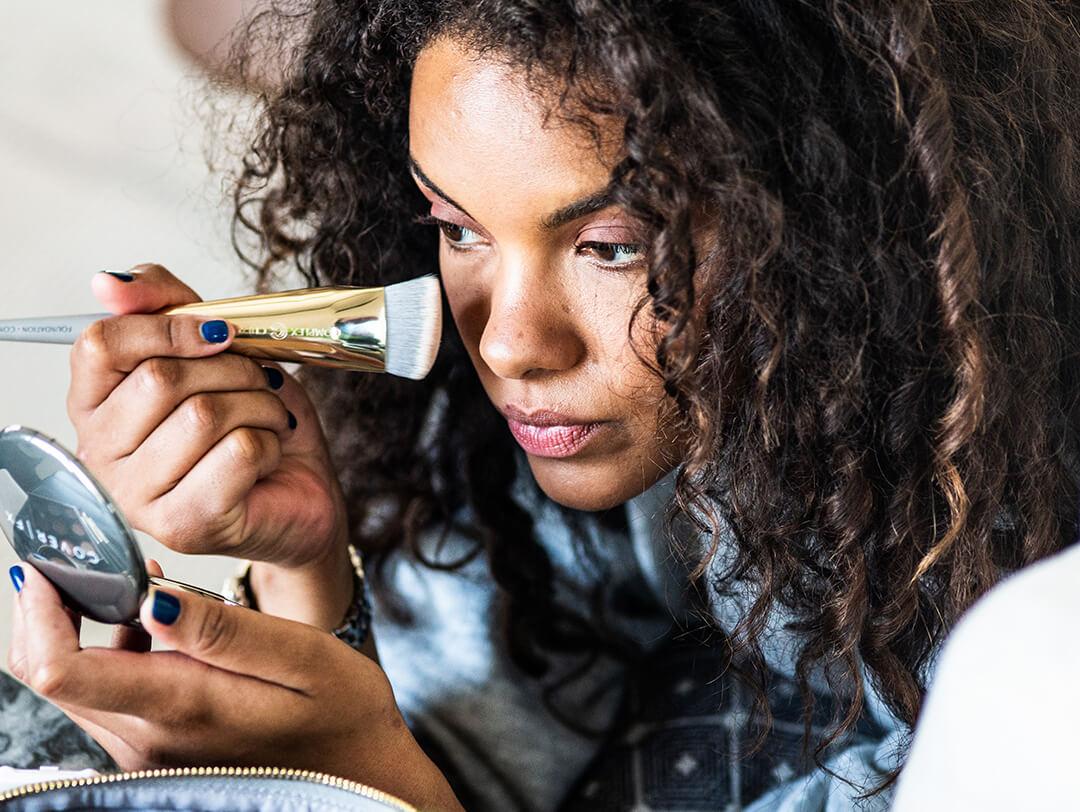 Image of a curly woman applying a cosmetic product on her face using a fluffy brush Desktop