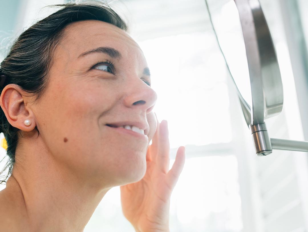 A photo of a woman applying face cream in front of a round mirror Desktop