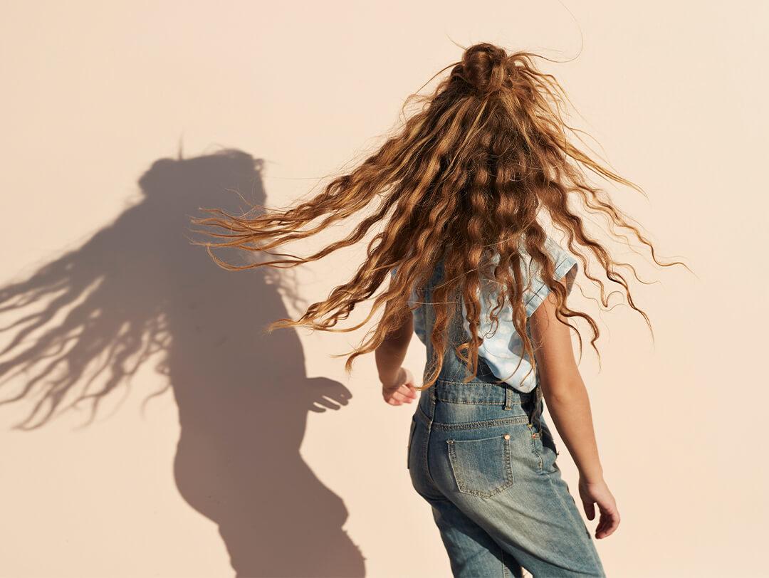 Image of a girl in a denim jumper and light blue shirt with her wavy hair in the air Desktop