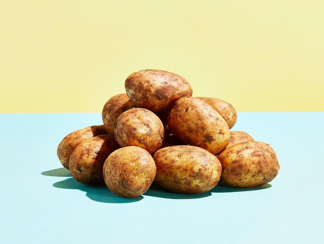 Pile of potatoes on top of light blue surface with light yellow background Desktop