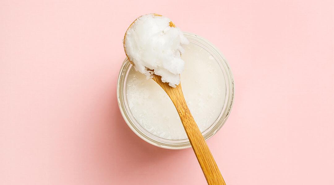 Small bowl of coconut oil and wooden spoon on pink background Desktop
