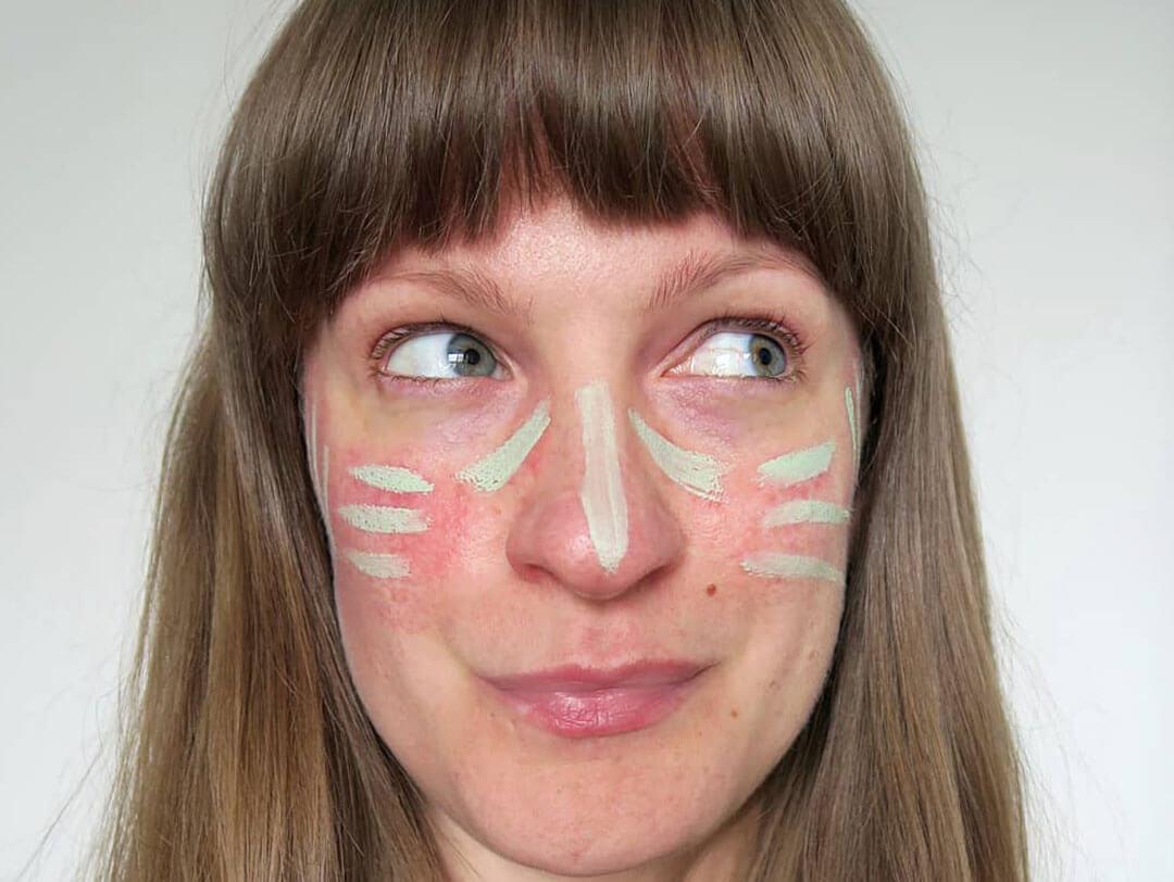 A close-up shot of a woman with bangs, her gaze directed to the side, featuring areas of green concealer on her face Desktop