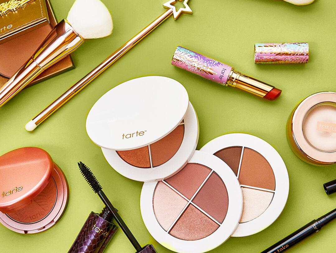Various beauty and makeup products from TARTE scattered on green background Desktop