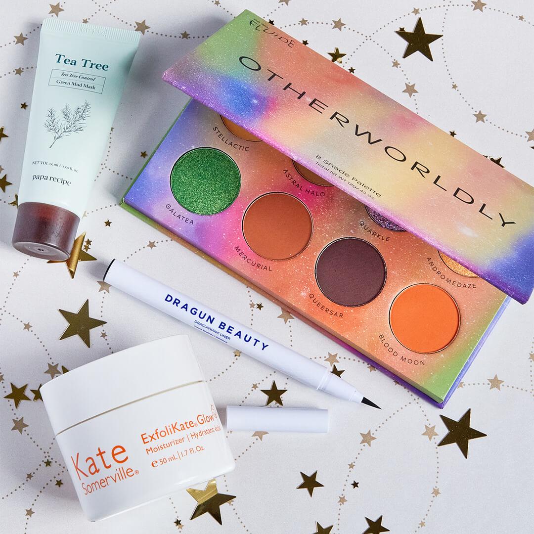 Beauty products from various brands on white paper with gold stars print Desktop