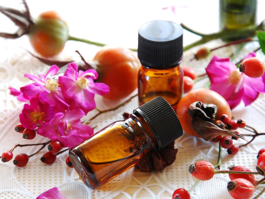 Small jars of essential oil and red and pink flowers on white cloth Desktop