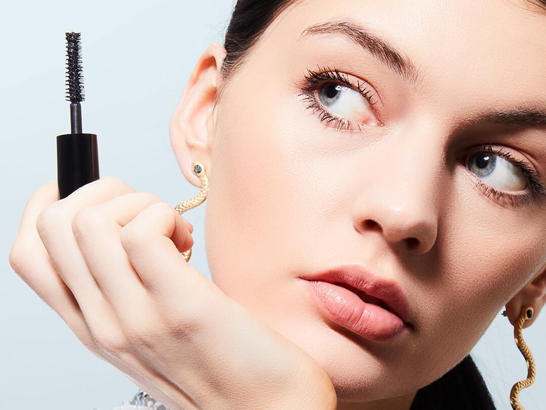 Studio portrait of a model holding up and looking at a mascara Desktop