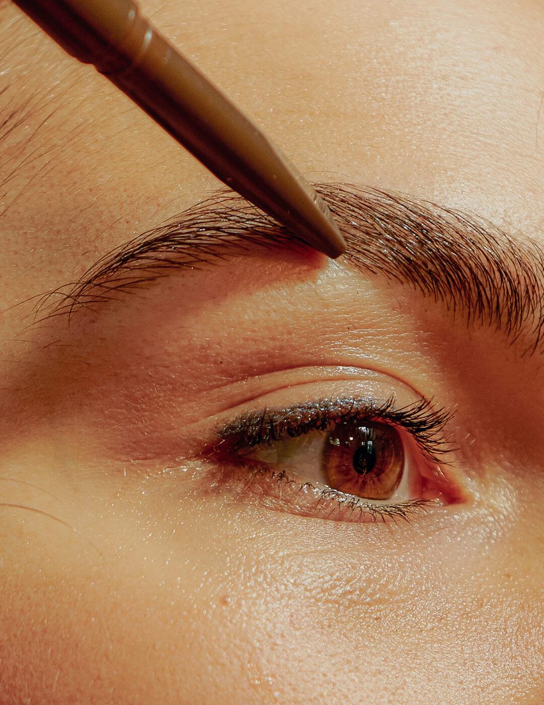 A photo of a woman's eye with a brown brow pencil on her eyebrow Mobile