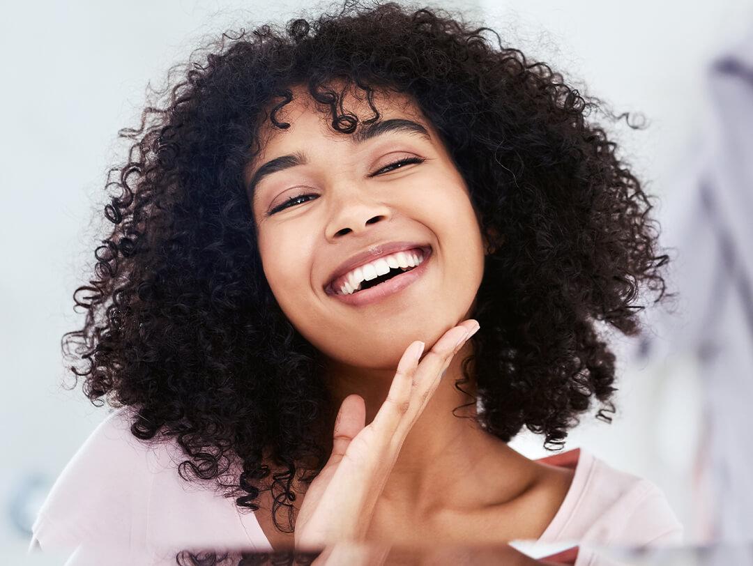 Young woman with curly hair smiling while holding her chin Desktop