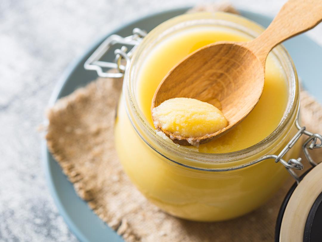 A photo of beef tallow in a jar and wooden spoon on gray table Desktop