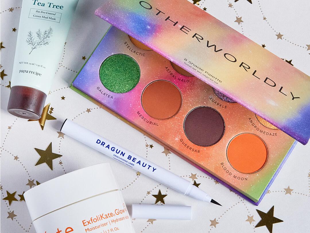 Beauty products from various brands scattered on white paper with gold stars print Desktop