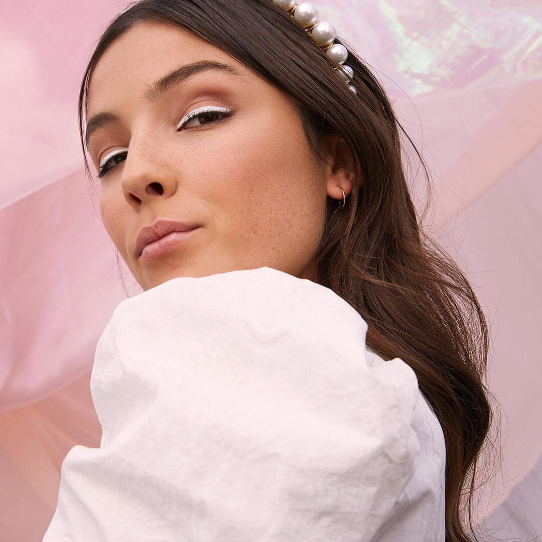 Close-up image of a model rocking a white eyeliner look and pearl-studded headband Desktop