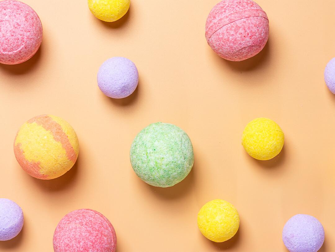 Bath bombs of different sizes and colors on yellow background Desktop
