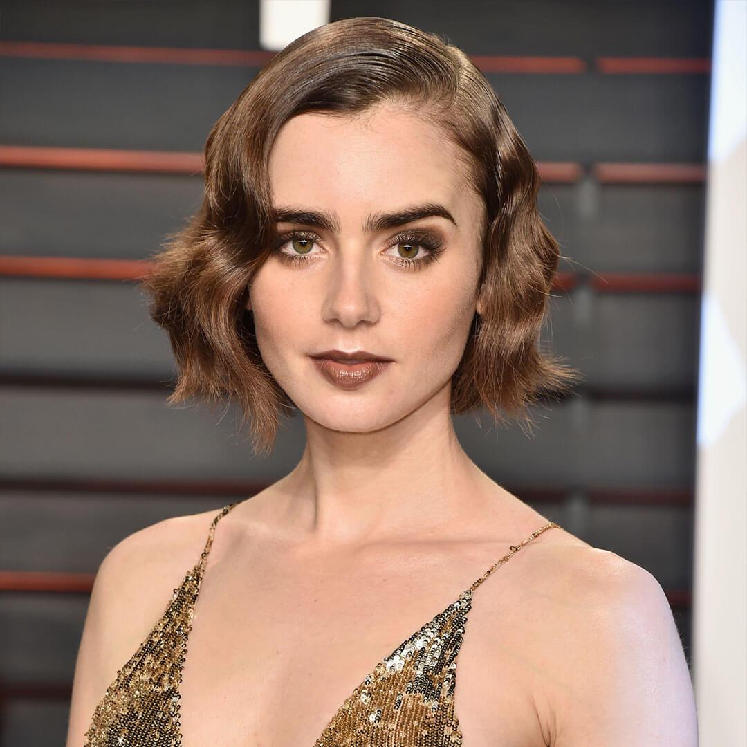An image of Lily Collins, with her Retro Glam Monochromatic Makeup wearing a gold sequined plunge halter top dress staring straight at the camera Mobile