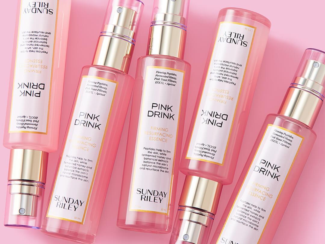 Bottles of SUNDAY RILEY Pink Drink Firming Resurfacing Essence on pink background Desktop