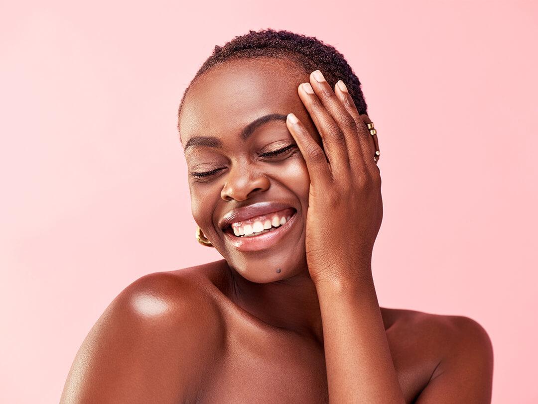Studio portrait of a smiling Black woman with very short hair posing against pink background Desktop
