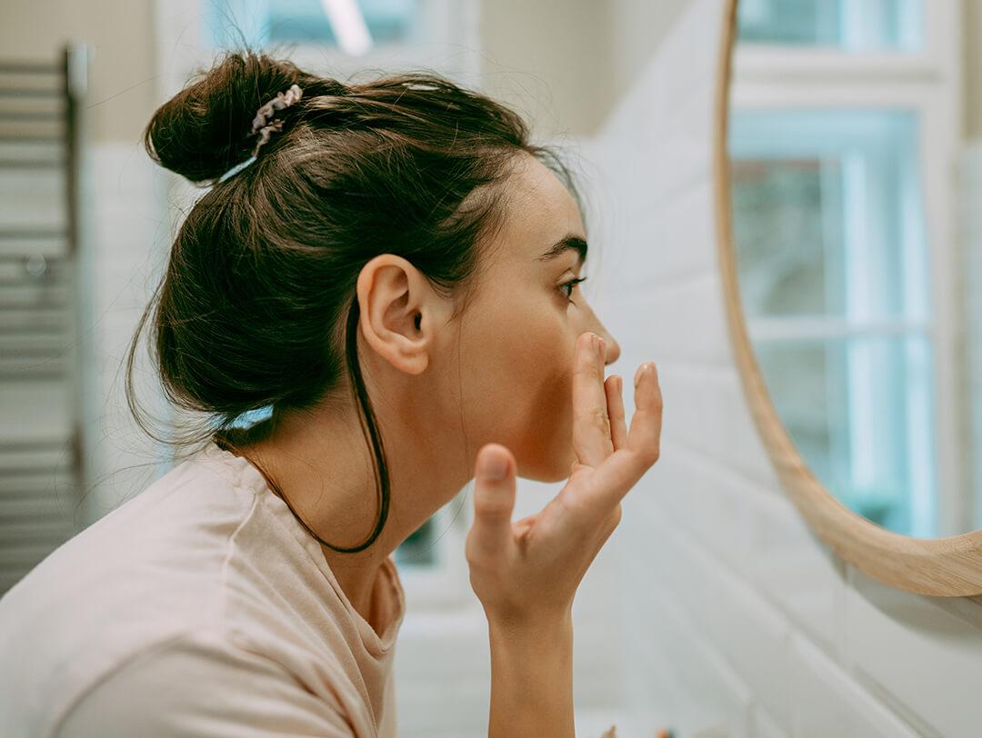 A photo of a woman applying moisturizer on her face in front of a mirror in the bathroom Desktop