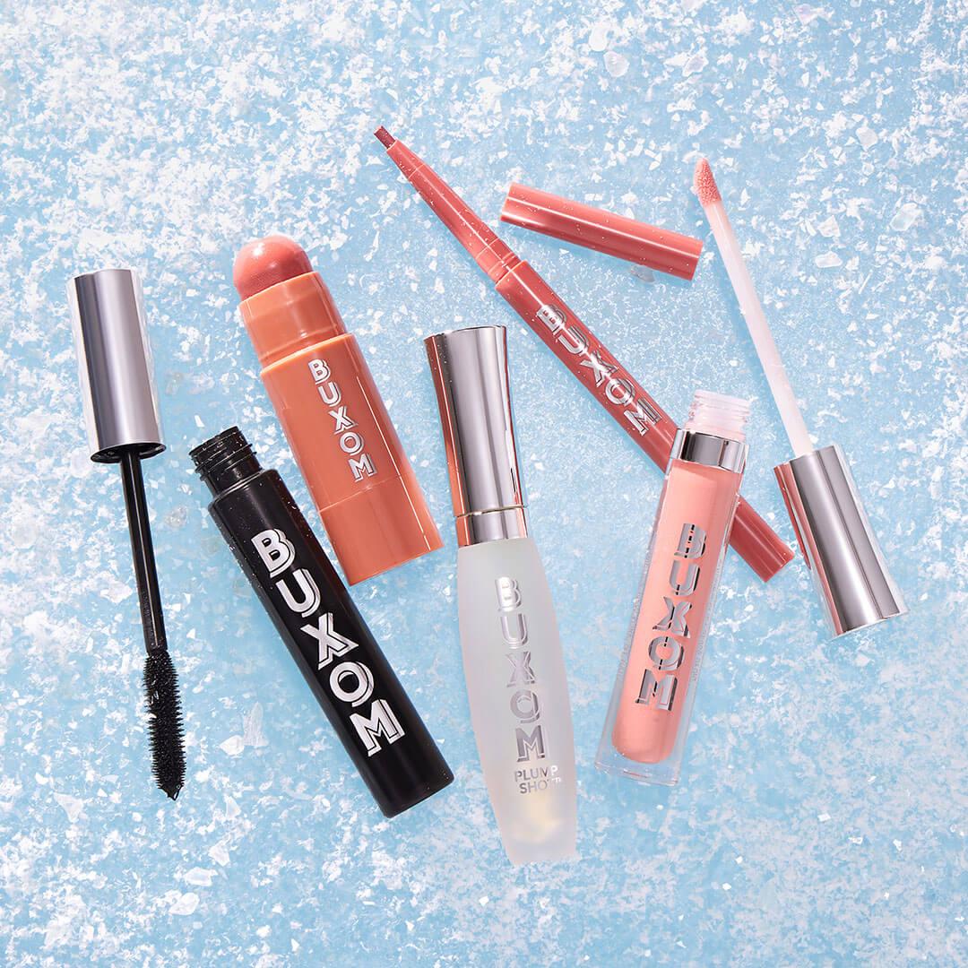 BUXOM COSMETICS Holiday Bundle product scattered on glittery blue surface Desktop