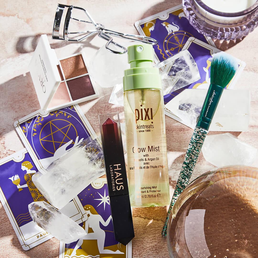 Flat lay image of skincare, makeup products and tools, crystals, and tarot cards on rose gold cloth Mobile